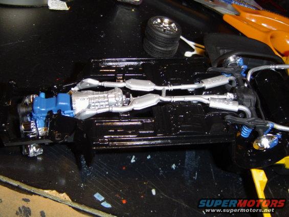 model car chassis with blue engine and silver exhaust system, plus a separate tire