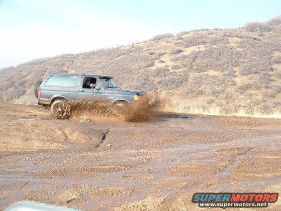 Gray 1991 Ford Bronco driving through mud, splashing water