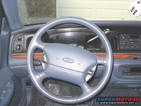 Ford steering wheel and dashboard with wood trim. Dice hanging from rearview mirror