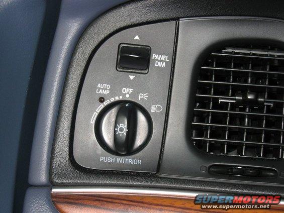 Car interior showing dashboard light controls with 'AUTO LAMP', 'OFF', 'PANEL DIM' labels and a rotary dial. Also visible is a black air vent