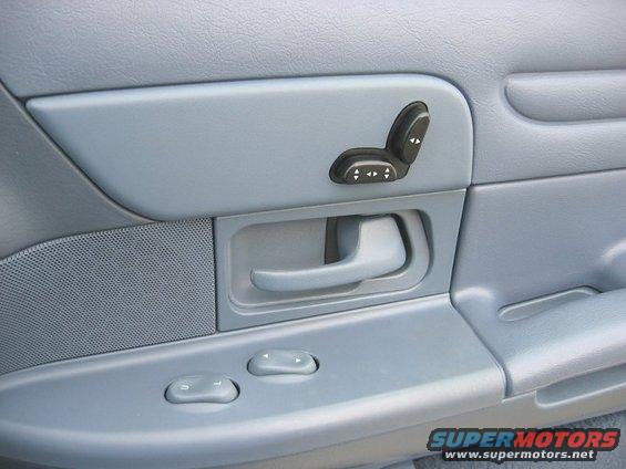Close-up of a car's interior door panel, showing power seat controls, door handle, and window controls