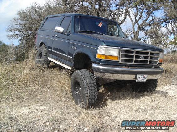 Dark blue Ford Bronco lifted with large tires, parked on a dry, grassy hill
