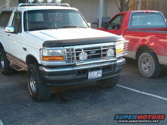 White Ford Bronco, front view, chrome grille guard, roof lights, aftermarket wheels, brown trim
