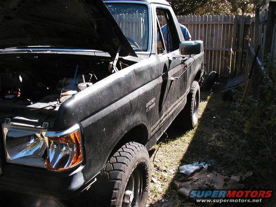 Black 1989 Ford Bronco with hood open, parked outside next to a wooden fence