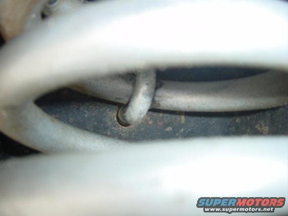 Close-up of a white suspension coil spring with a metal clip. Part of a vehicle's undercarriage