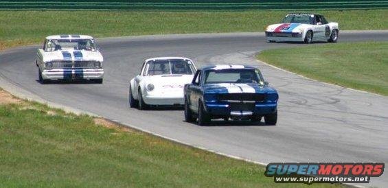 Blue 1965 Ford Mustang and white Porsche race on track with other cars