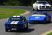 1965 Ford Mustang - A blue 1965 Ford Mustang races on a track alongside other vehicles, captured from a front-facing perspective.
