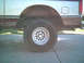 1988 Ford Bronco - Side view of a silver truck's rear wheel well and tire, with visible rust and mud on the fender.