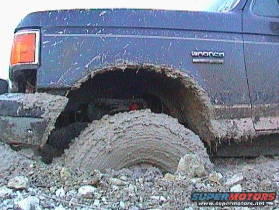 1989 Ford Bronco stuck deep in mud, front fender and wheel visible