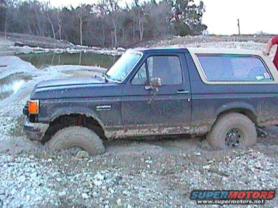 Ford Bronco stuck in mud, front wheel deep in muck. Beige top