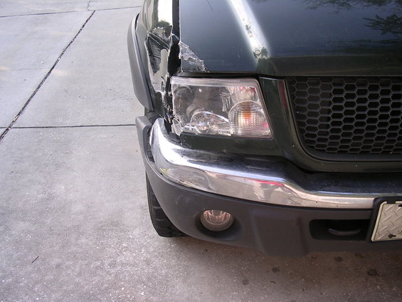Damaged dark green pickup truck front end with dented fender and broken headlight