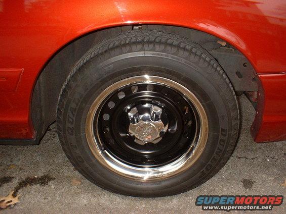 Orange car fender over a black steel wheel with a chrome trim ring and chrome hubcap. Dunlop tire