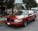 1999 Ford Crown Victoria - This red Ford Crown Victoria sedan is parked on a street in front of a house. The view is from the front three-quarter angle.