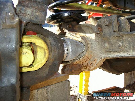 Close-up of a yellow driveshaft U-joint connected to a differential housing with a black coil spring above