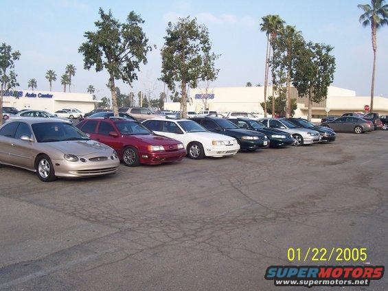 Several sedans parked in a lot in front of a Sears Auto Center