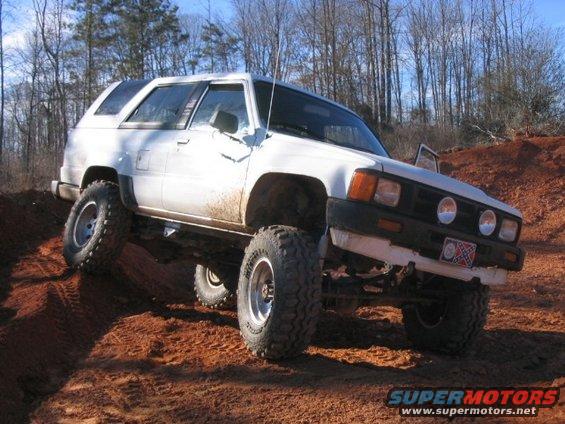 White SUV with large tires on a dirt hill. Has a Confederate flag license plate
