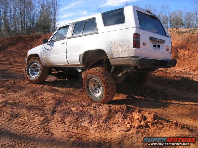 White Toyota 4Runner with lifted suspension driving on muddy terrain