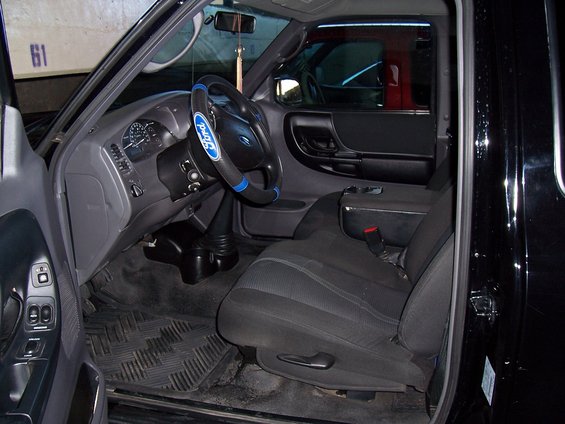 Interior of a Ford Ranger pickup truck, showing the driver's seat, dashboard, steering wheel with Ford logo cover, and center console