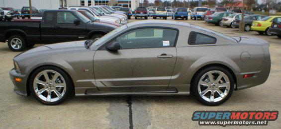 Side view of a gray Ford Mustang parked in a lot with a black pickup truck behind it