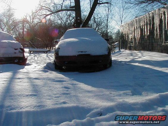 Two cars covered in snow, front view. Icicles hang from a building