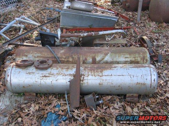 Scrap metal tanks and parts piled on the ground among fallen leaves