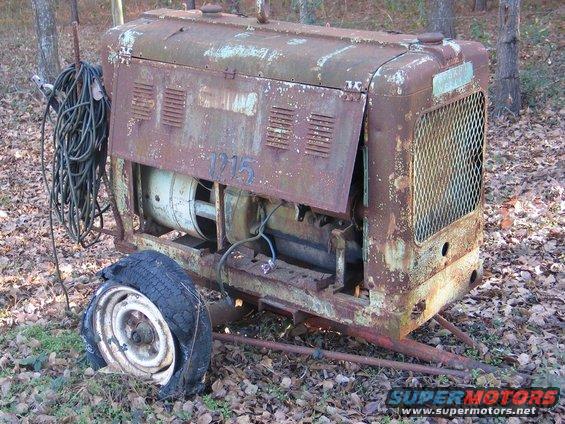 Rusty welding machine with a flat tire and coiled cables. Number '1215' is painted on the side