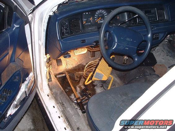 1996 Ford Crown Victoria interior showing dashboard, steering wheel, and driver's side door panel with tools and a work light on the floor