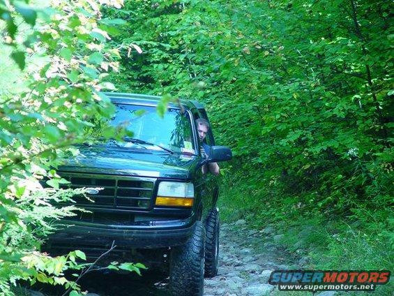 1996 Ford Bronco driving on a rocky, wooded trail. Driver is visible through the window