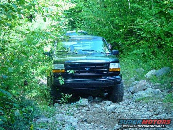 Black 1996 Ford Bronco on a rocky, wooded trail. Another vehicle is visible behind it