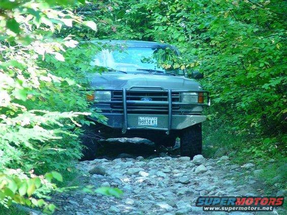 Dark green Ford Bronco with a brush guard on a rocky, wooded trail