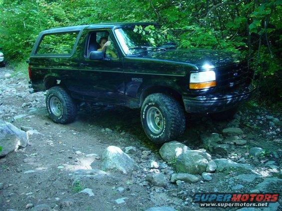 Black 1996 Ford Bronco driving on a rocky trail through trees