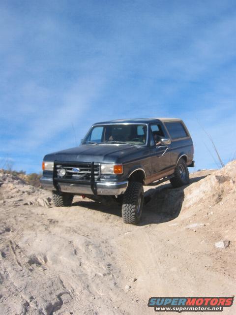 Dark blue Ford Bronco on a dirt hill, front grille and bumper visible