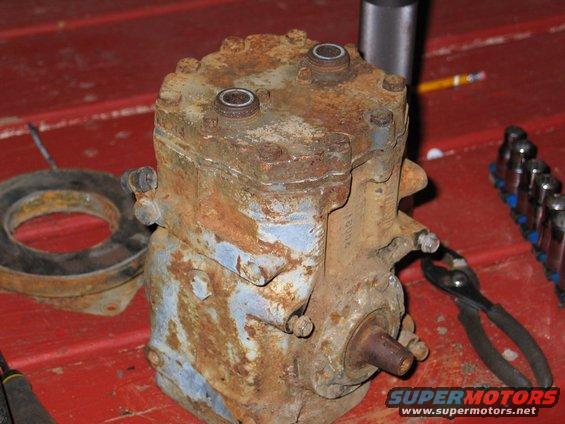 Rusty air conditioning compressor with a gasket and tools on a red surface
