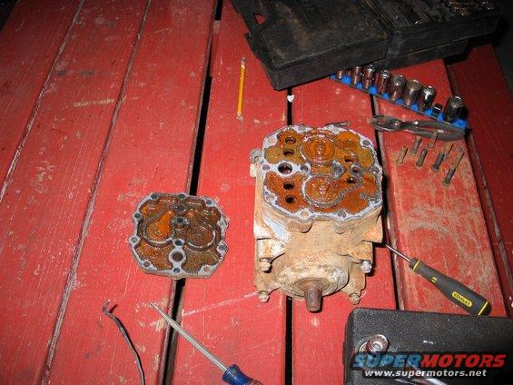 Two heavily rusted engine components and tools on a red wooden surface