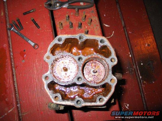rusted engine part with two circular openings, on a red wooden surface with tools
