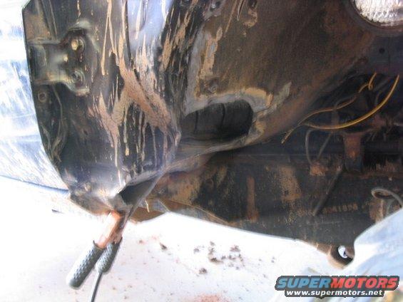 Mud-splattered black metal frame and suspension parts, with visible wiring and a part number