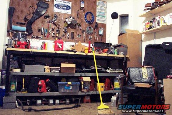 Garage workbench with tools, supplies, and a Ford logo sign on the pegboard