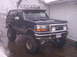 1993 Ford Bronco - A dark-colored, lifted 1993 Ford Bronco is parked in front of a garage on a wet, overcast day.