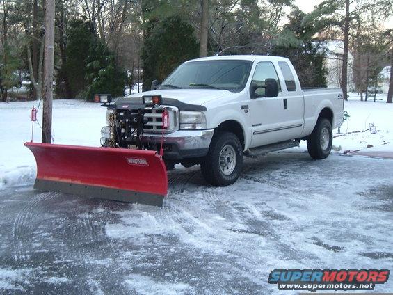 White Ford F-250 truck with a red snow plow attached, parked on a snowy driveway