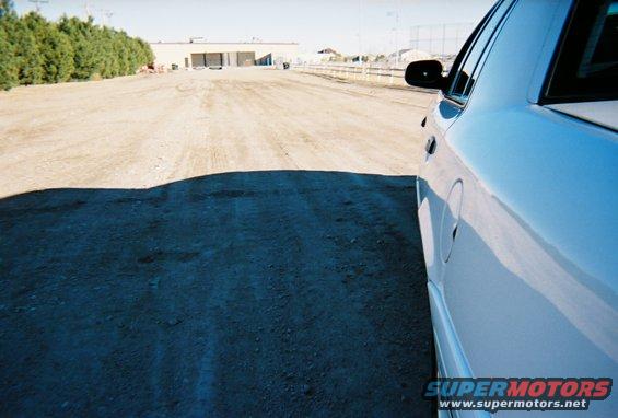 Side view of a white sedan parked on a dirt lot