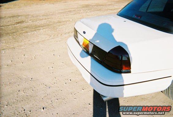 White 2000 Ford Crown Victoria rear quarter panel with dark tinted taillights and a shadow of a person