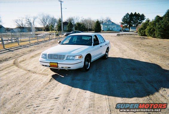 White 2000 Ford Crown Victoria sedan on a dirt road, front 3/4 view, slight damage to front bumper