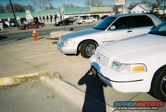 Two white Ford Crown Victoria police cars parked side-by-side. The one in front is closer to the camera