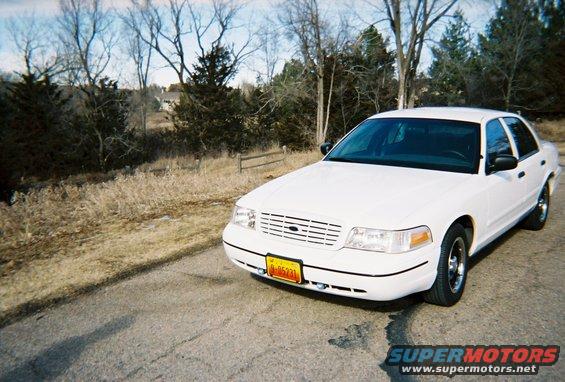 White 2000 Ford Crown Victoria sedan parked on a paved road, front 3/4 view. License plate is yellow with black text