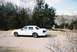 2000 Ford Crown Victoria - A white 2000 Ford Crown Victoria is parked on the side of a road with trees and a body of water in the background.