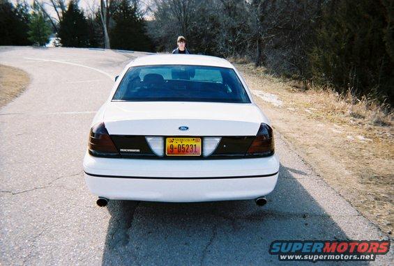 White 2000 Ford Crown Victoria sedan, rear view, on a paved road with trees