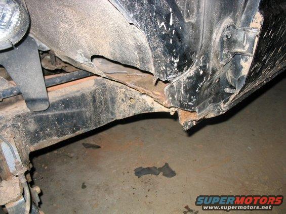 Black truck frame and fender showing rust and damage. Visible headlight assembly
