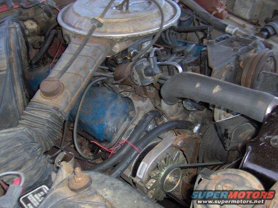 Engine bay with air cleaner assembly, alternator, and hoses visible. Some text on alternator