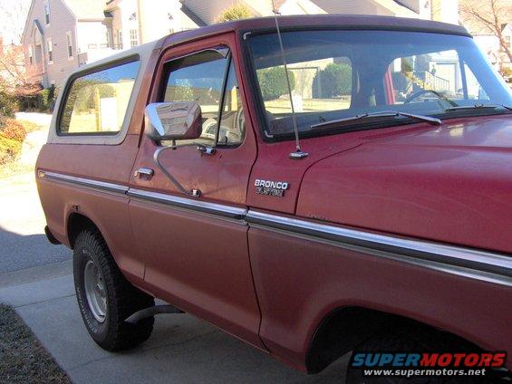 Side view of a red 1978 Ford Bronco with a tan top. The 'Bronco' badge is visible on the fender