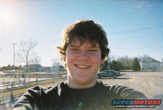 Person taking a selfie outdoors with a gray sedan parked in the background